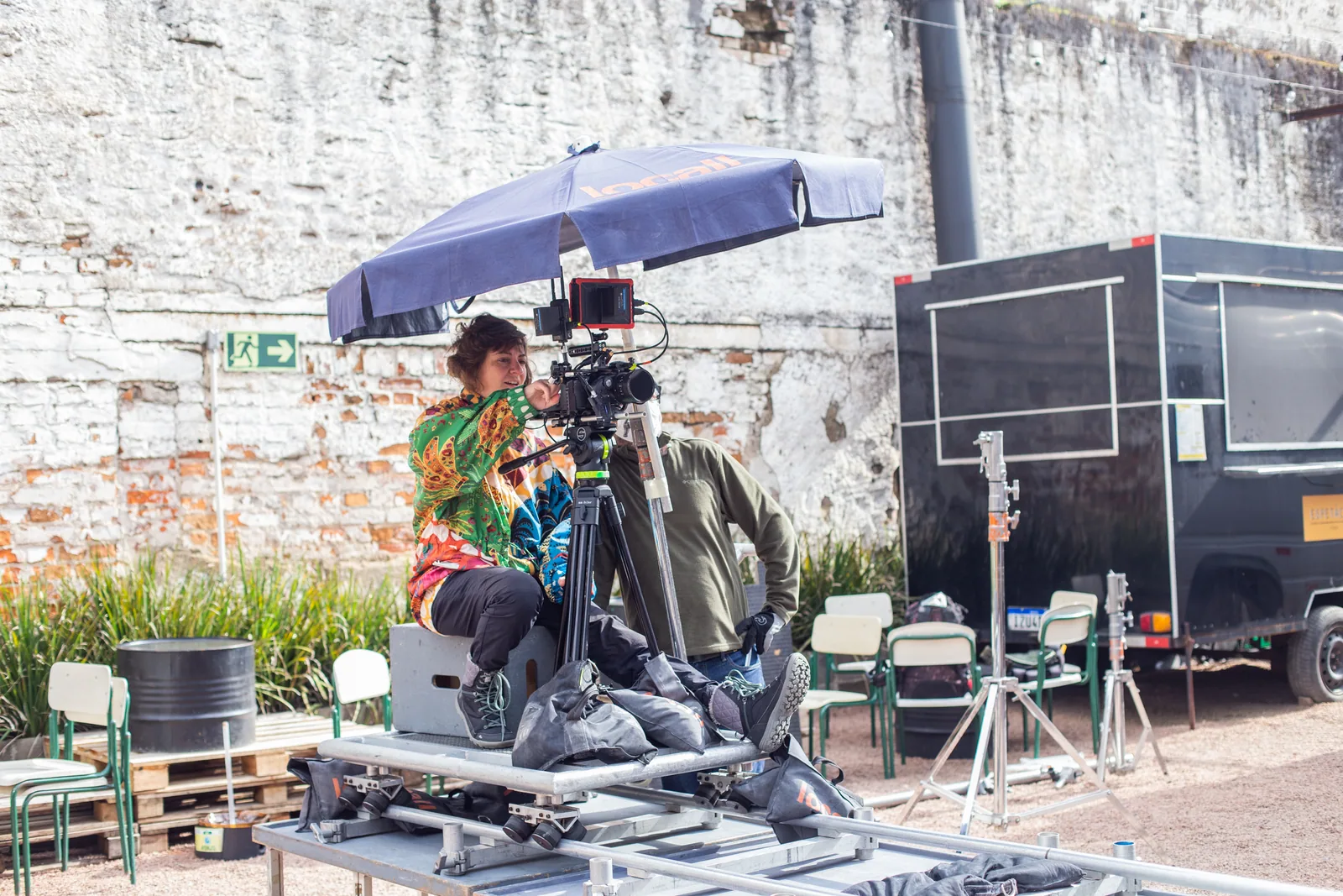 Cinematographer seated behind a camera on a dolly track, under a parasol